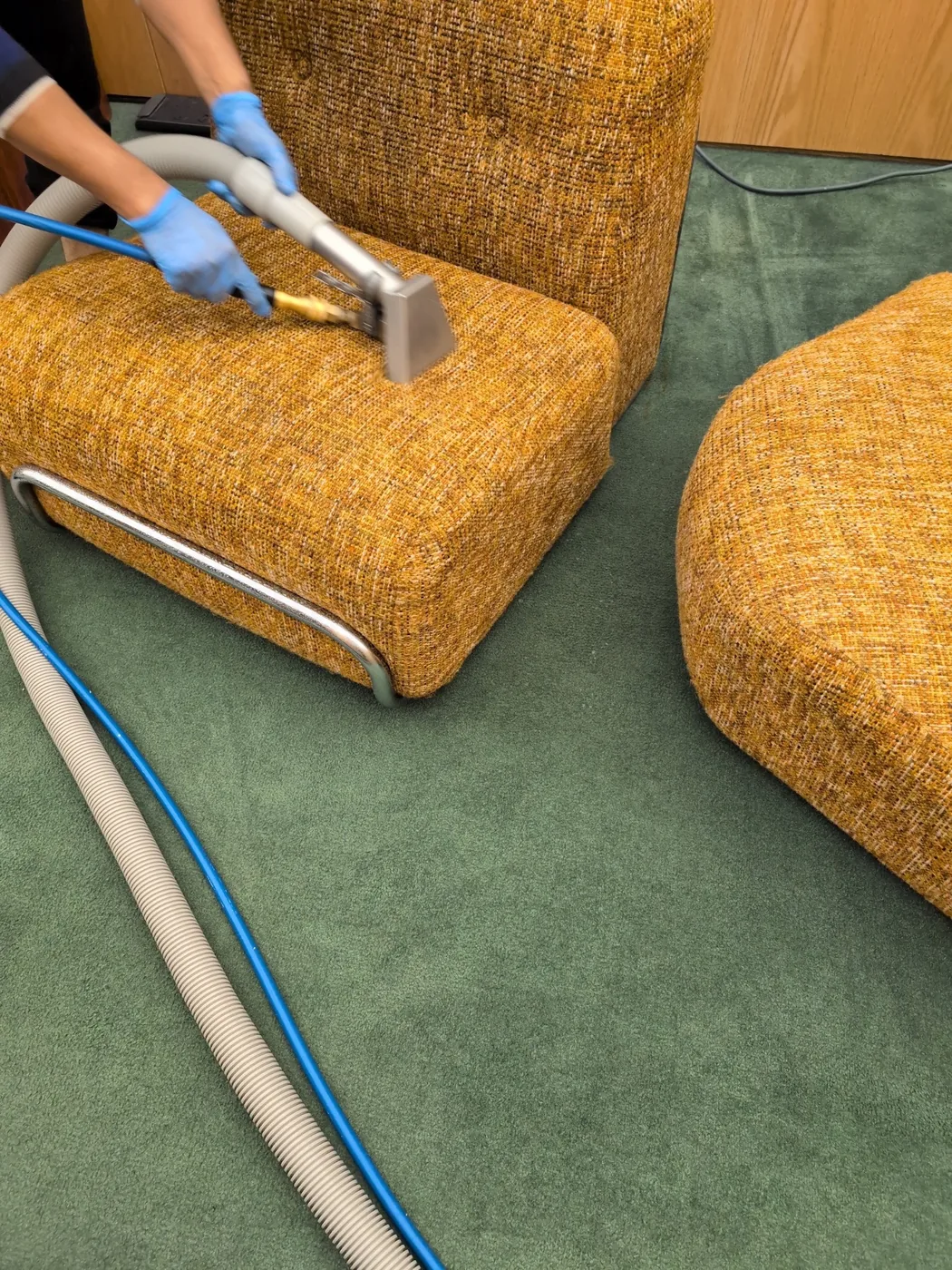 Gloved hands cleaning an orange upholstered chair