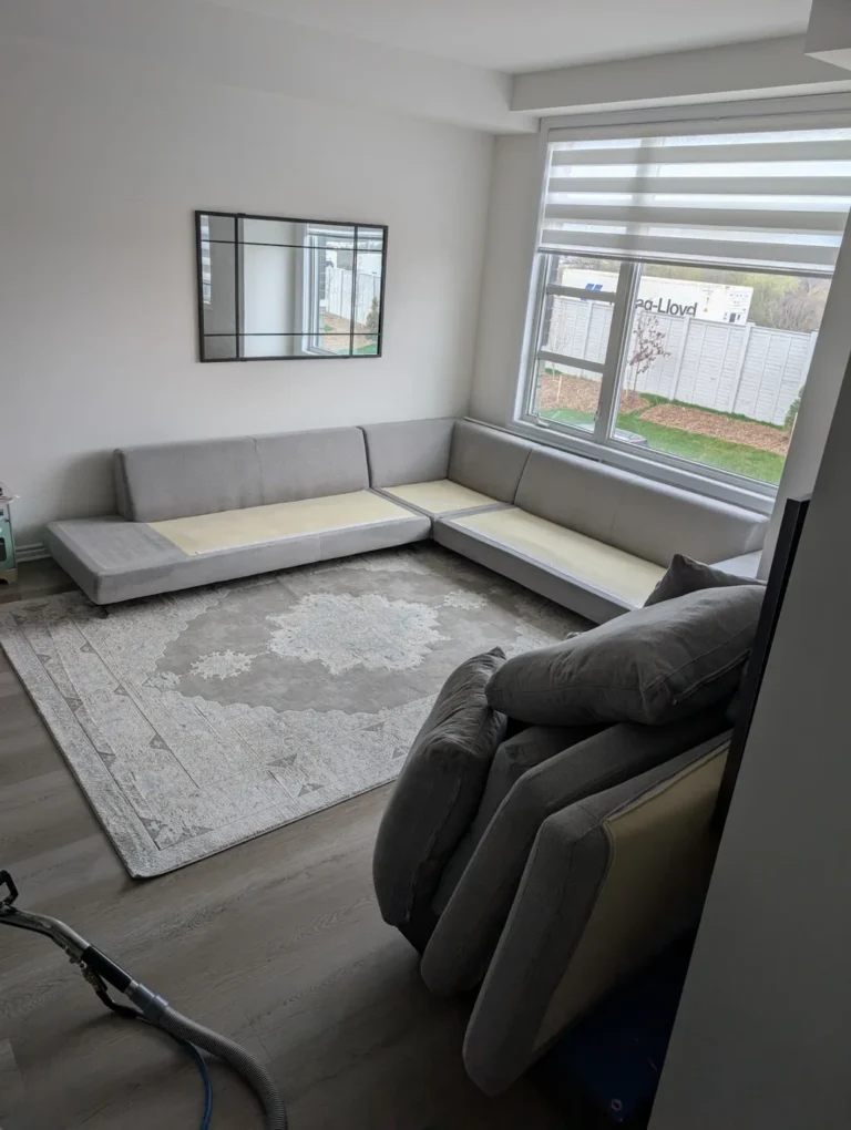 Grey sectional sofa with cushions removed and a cleaning wand nearby